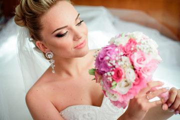 Naklejka premium Charming blonde bride sits on the floor with wedding bouquet in her arms