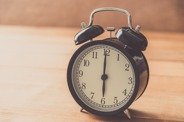 black alarm clock on wood table , vintage tone