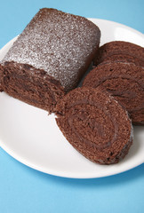 A close up of a sliced chocolate Swiss roll cake on a bright blue background