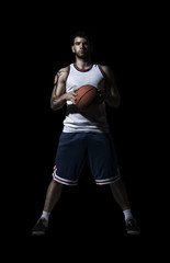 basketball player standing in durkness with ball on black isolated