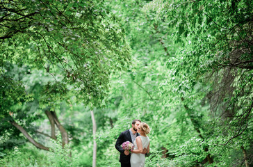 Fototapeta na wymiar Tender wedding couple stands kissing among tall green trees