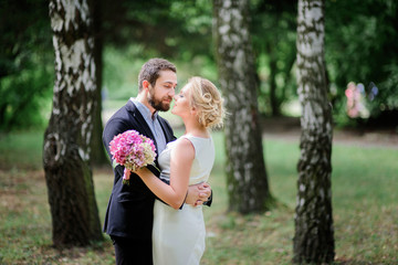 Fototapeta premium Bearded groom hugs tender blonde bride while she holds pink wedding bouquet