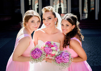 Stunning blonde bride and bridesmaids lean to each other posing in the rays of morning sun