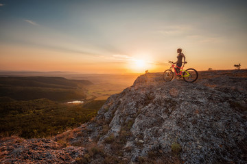 Naklejka na ściany i meble Active life / A woman with a bike enjoys the view of sunset over an autumn forest