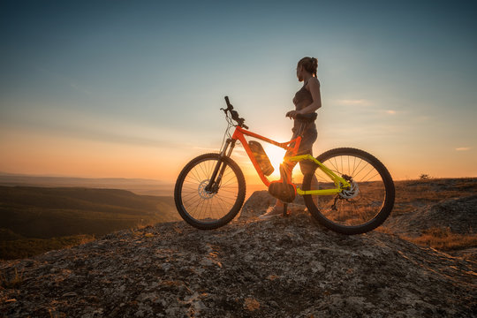 Active life /
A woman with a bike enjoys the view of sunset over an autumn forest