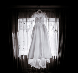 Long wedding dress with lace top hangs before window