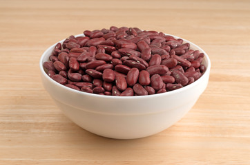 Bowl filled with dark red organic kidney beans atop a wood table.