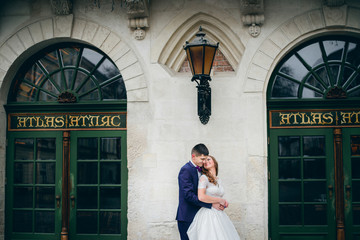 Bride and groom lean to each other tender standing under the lantern on white house