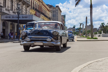 Schwarzer Oldtimer mit weißem Dach fährt auf der Hauptstraße an der historischen Häuserfront vorbei - Serie Kuba Reportage