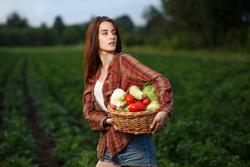 A young woman holding a basket of freshly harvested vegetables in her vegetable garden