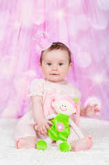 Girl with a crown, sitting on a pink background with bokeh.