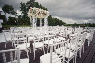 White chairs stand in rows before white wedding alrar decorated with rich garland of roses