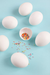 Naklejka na ściany i meble Easter decoration white chicken eggs and broken egg with colored sugar ingredients on a light blue background, vertical image