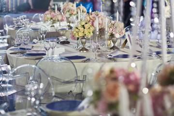 Rich dinner table decorated with pink rose bouquets, silver candleholders and served with blue plates