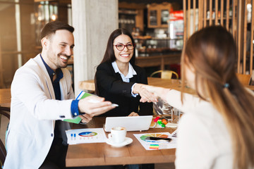 Young business people gathered at table, making deal signing contract shaking hands after paper work.