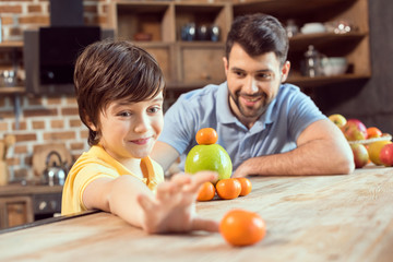 Fototapeta premium Happy father and son playing with citrus fruits in kitchen