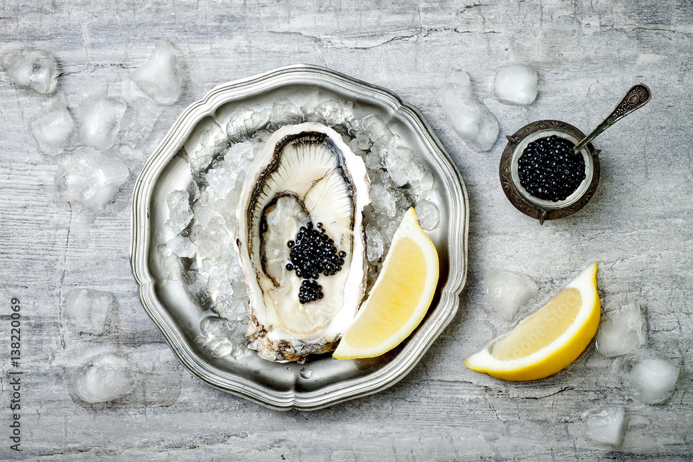 Wall mural opened oyster with black sturgeon caviar and lemon on ice in metal plate on grey concrete background