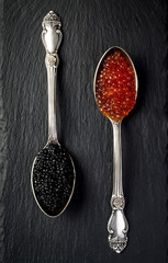 Two vintage silver spoons with red salmon and black sturgeon caviar on black slate stone...