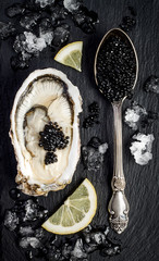 Vintage silver spoon with black sturgeon caviar and oyster on black slate stone background. Top...