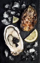 Oysters with black sturgeon caviar and lemon on black slate stone background. Top view, flat lay