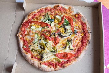 brown cardboard box open with vegetarian pizza, with vegetables like eggplant, zucchini, corn, red and green pepper, onion, tomato and cheese
