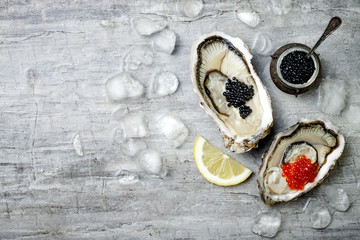 Opened oysters with red salmon and black sturgeon caviar and lemon on ice on grey concrete background. Top view, flat lay, copy space - obrazy, fototapety, plakaty