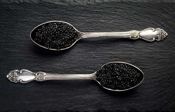 Two vintage silver spoons with black sturgeon caviar on black slate stone background. Top view, flat lay, copy space