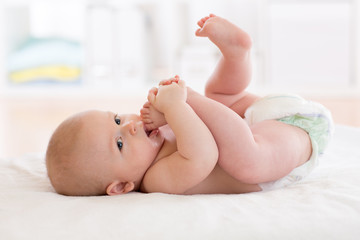 baby boy lying on white sheet with foot in mouth