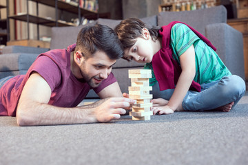 smiling father and focused son playing jenga game at home