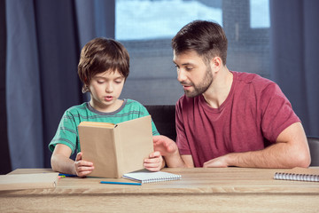 portrait of father helping concentrated son reading book