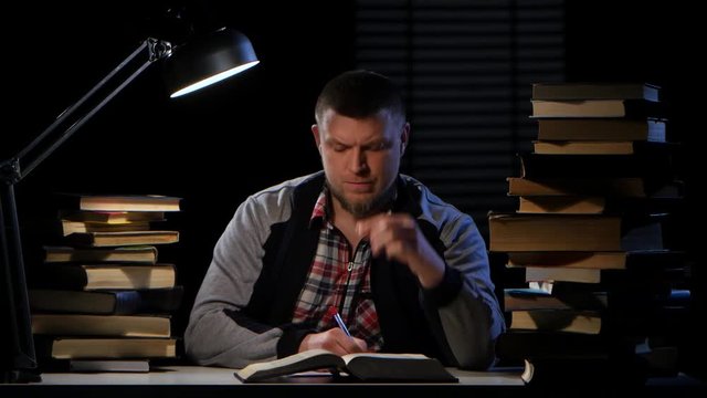 Guy in the light of the lamp he reads terribly headache. Black background