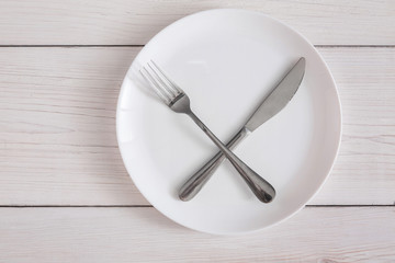 Empty plate with crossed fork and knife on white wood top view