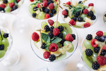 The vase with grapes,raspberries,kiwis and blackberries  stand on the buffet table