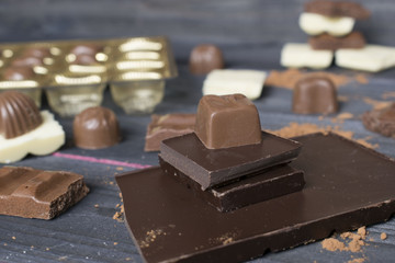 chocolate composition, box of chocolates, bar of chocolate, pieces of chocolate and some cocoa powder on the grey wooden background.