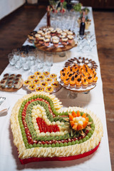 The different cakes and heart of fruits stand on the buffet table