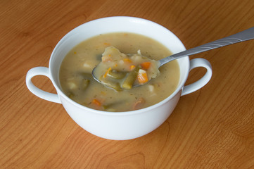 Vegetable soup and silver spoon in a white bowl on wooden background.