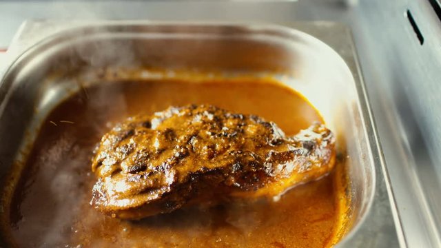 Rotating of hot meat dishes with pork with gravy boiling sauce at restaurant kitchen