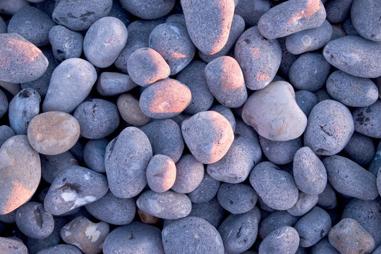 grey pebbles on beach at sunset with pink glow grom sunset on some of the pebbles
