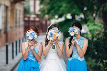 The bride with bridesmaids keep bouquets and stand in the street