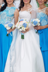The bride with bridesmaids keep bouquets and stand in the street