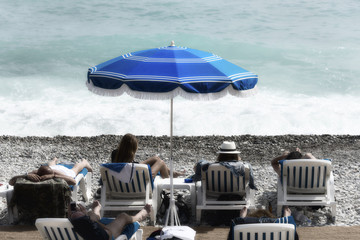 tourists, sunbeds and umbrellas on summer hot day. mediterranean sea beach in Nice, France.