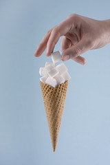 Zuckerkonsum / Hand greift nach Würfelzucker in Eistüte