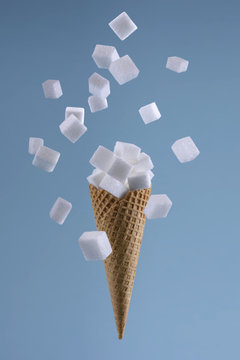 erh&ouml;hter Zuckerkonsum / Eiswaffel mit herabfallendem W&uuml;rfelzucker