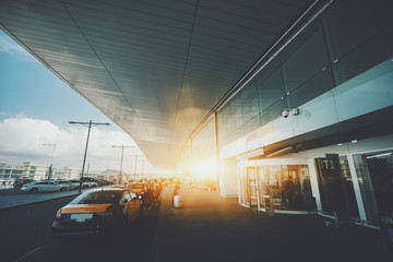 Entrance of modern contemporary airport terminal in Barcelona with multiple cars around, many taxis, moving blurred people with their luggage on sunny summer day