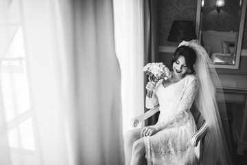 beautiful and young bride in veil with bouquet of flowers sitting on the chair