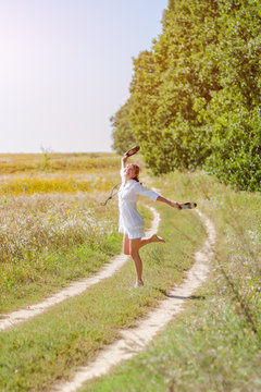 Young beautiful woman running in grass barefoot and holding shoes in hands