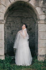 beautiful and young bride in white dress and veil standing outdoors