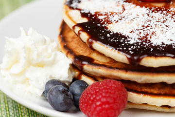Pile of Pancakes with blueberries and raspberries, chocolate sauce and powder sugar