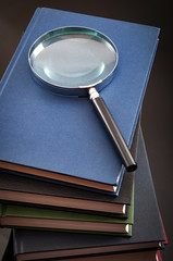 Research and fact checking concept with a magnifying glass on top of a stack of books