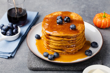 Pumpkin pancakes with maple syrup and blueberries on a plate. Grey stone background